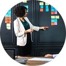 a woman pointing to sticky notes lined up on a wall