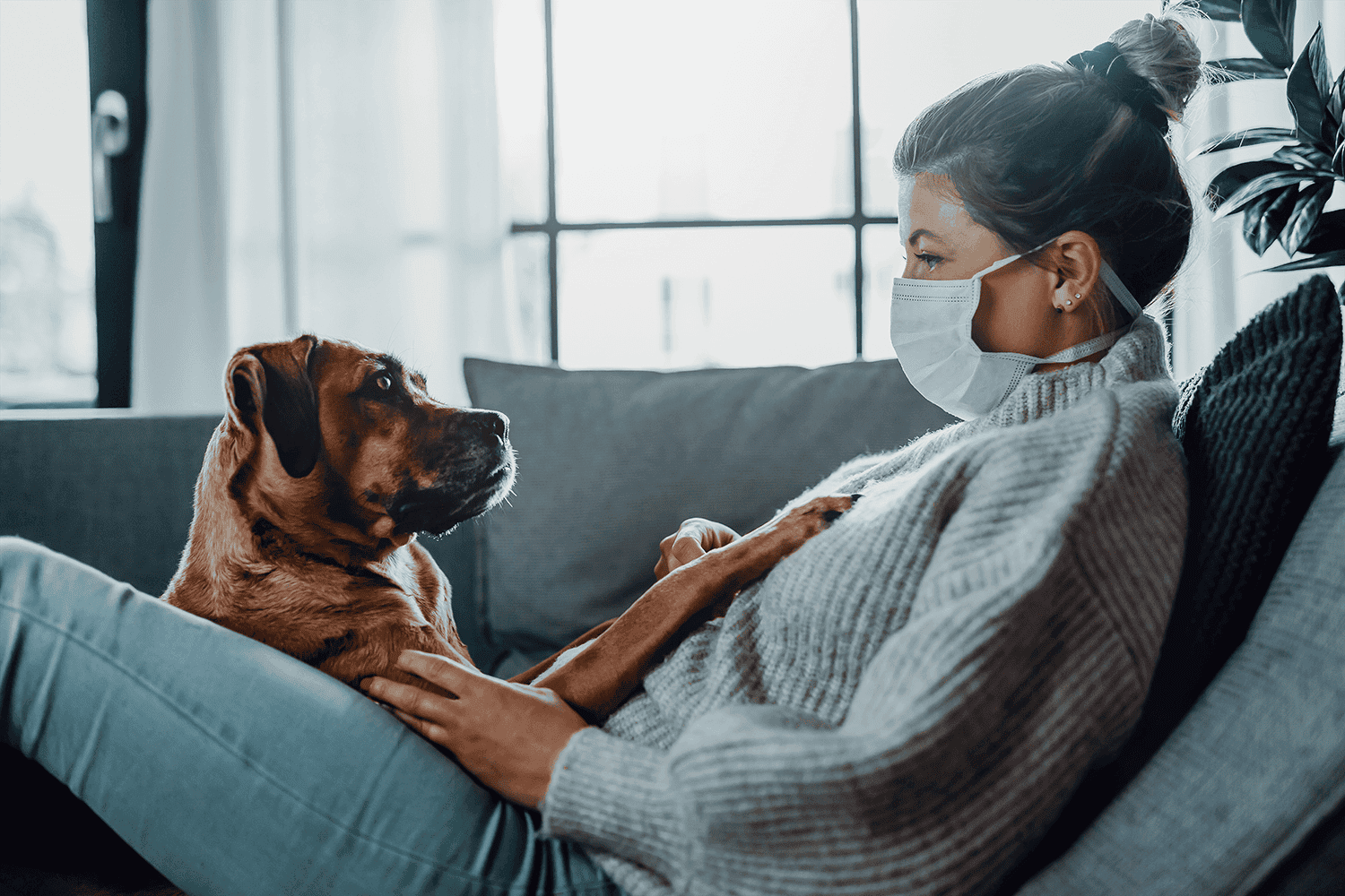 woman wearing a face mask sitting on a couch with her dog