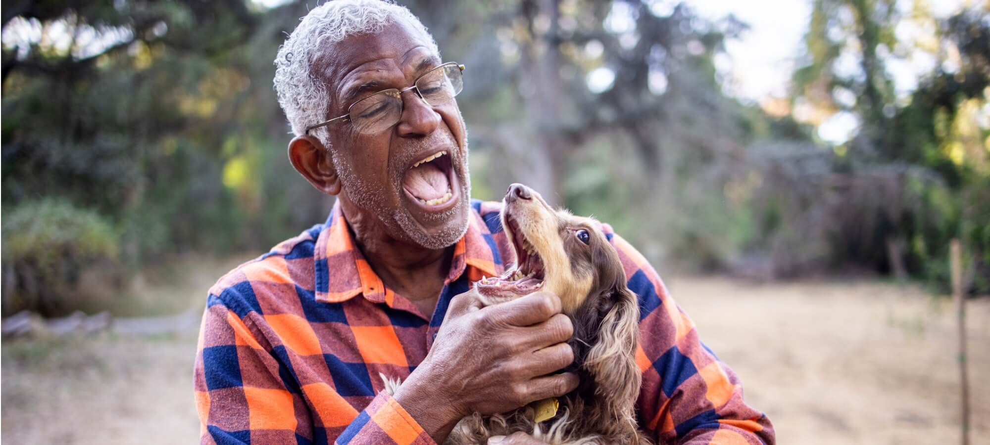 senior black man with long haired dachsund, both with their mouths open having a good time