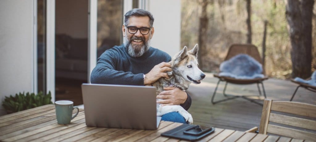 older man with dog seated outdoors in front of a laptop