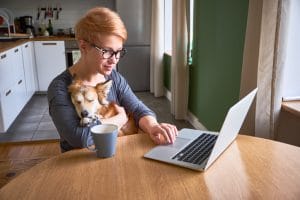 Person sitting at a table in front of an open laptop, with a dog relaxed and sleeping in her arms