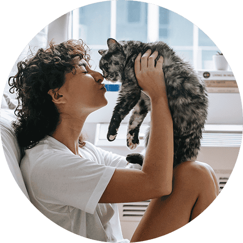A woman holding up her cat in front of her and giving it kisses.