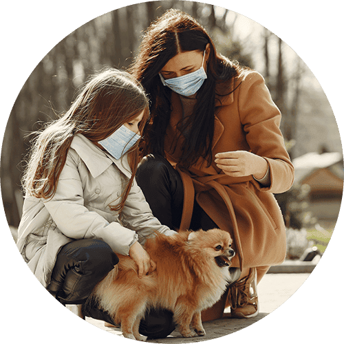 A mother and daughter wearing masks, standing outside with their dog.