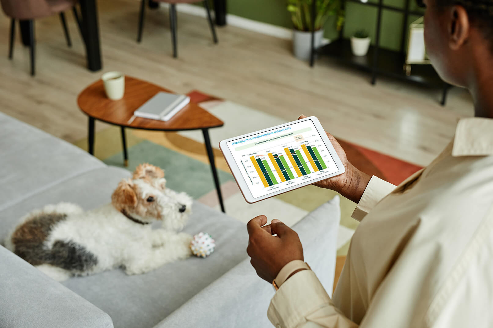 person holding tablet displaying bar graph, with a dog on the floor looking up at her